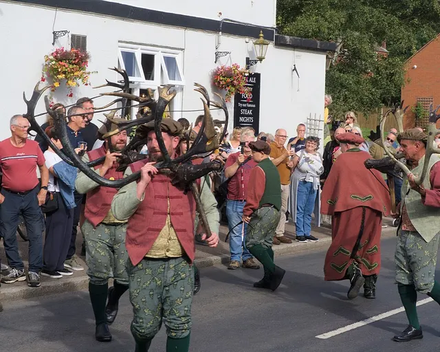 Deer-men carry antlers past a pub and a watching crowd during the Abbots Bromley Horn Dance procession.
