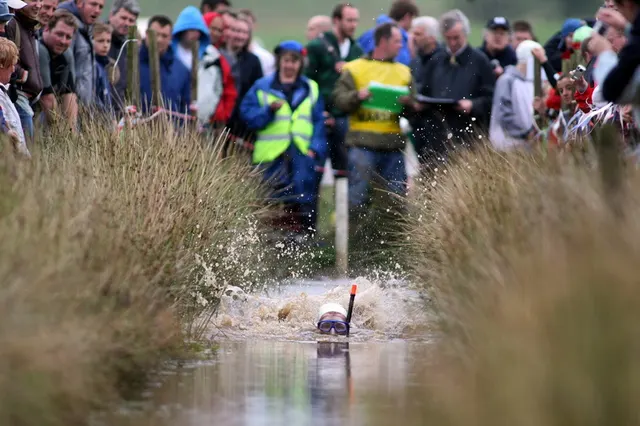 A snorkeller wearing flippers churns through a water-filled peat trench as onlookers watch from the bankside at the World Bog Snorkelling Championships.