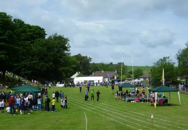 Spectators and competitors fill the Bow Butts field during Ceres Highland Games, marquees and cottages behind.