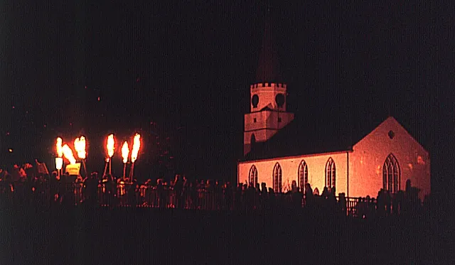 Lit torches, the Comrie flambeaux, glow beside the parish church on Hogmanay night.