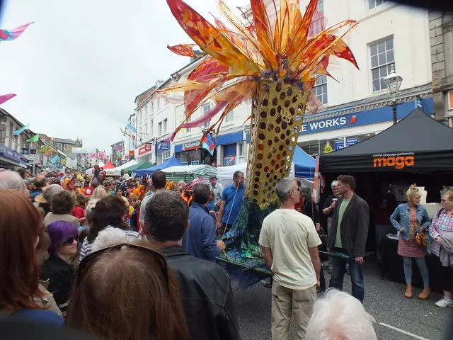 A giant flame-shaped parade puppet is carried above a crowd through Penzance during Mazey Day.