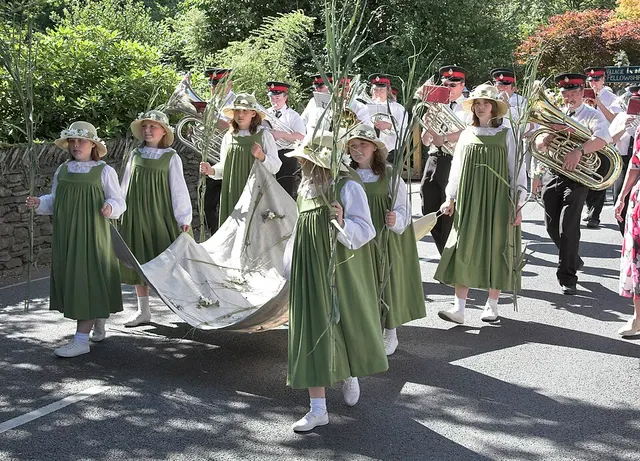 Girls in green pinafores carrying long rushes lead a brass band procession through Grasmere.