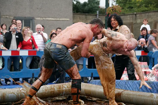 Two gravy-covered wrestlers grapple in a shallow pool as a crowd watches at the World Gravy Wrestling Championships.