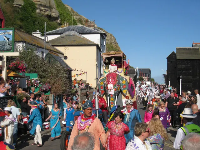 An elaborately decorated elephant float carries costumed performers through a crowd on Rock-a-Nore Road during the Hastings Old Town Carnival procession.