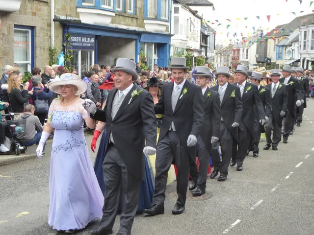 Couples in top hats and formal dress process along the street during the midday Furry Dance in Helston.
