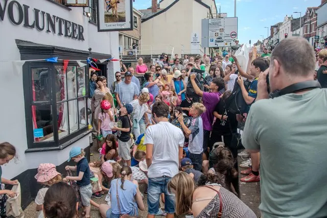 A crowd, including children, crouches to scramble for pennies outside The Volunteer pub during Honiton's Hot Pennies ceremony.