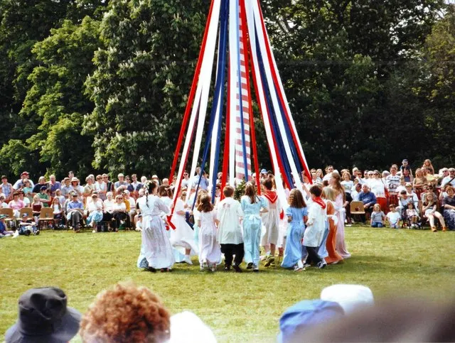 Dancers plait ribbons around the permanent maypole on Ickwell Green in front of a watching crowd.