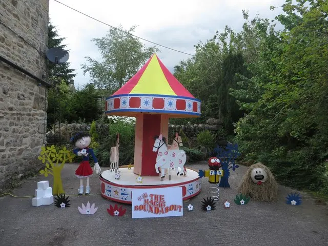 A homemade 'Magic Roundabout' scarecrow display with carousel horses and painted characters stands outside a house in Kettlewell.