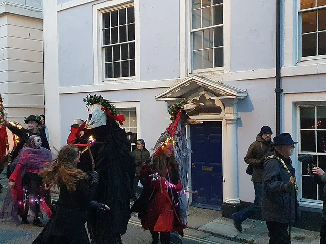 Costumed guise dancers in animal-skull masks and a veiled mask process past a Georgian townhouse during the Montol Festival in Penzance.