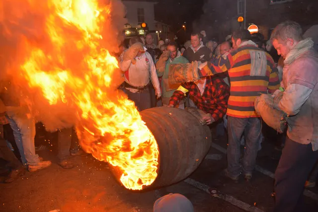 Men carry a blazing tar barrel through a crowd of spectators in Ottery St Mary.