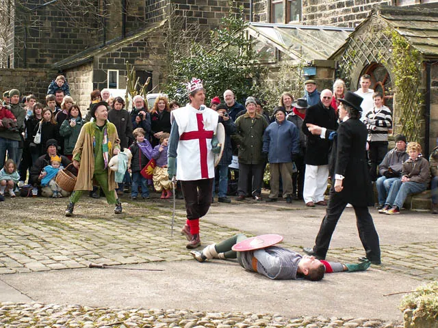 St George stands over a fallen Bold Slasher in the Heptonstall Pace Egg Play, watched by a crowd in Weavers Square.