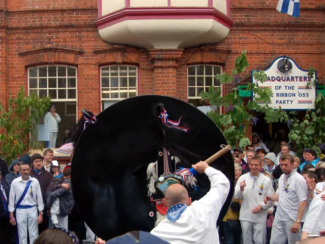 The Old 'Oss, led by a teaser and drummer, moves through a crowd of onlookers in the streets of Padstow on May Day.