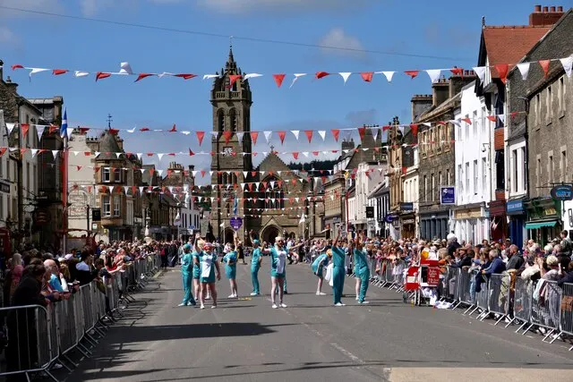 A costumed dance troupe performs in Peebles High Street beneath rows of bunting during the Beltane Festival.