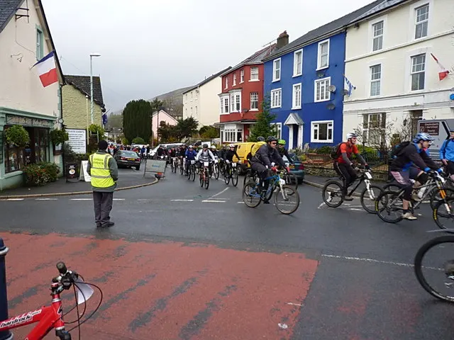 Cyclists ride out through Llanwrtyd Wells at the mass start of the Real Ale Wobble, a marshal in a Green Events vest directing them.