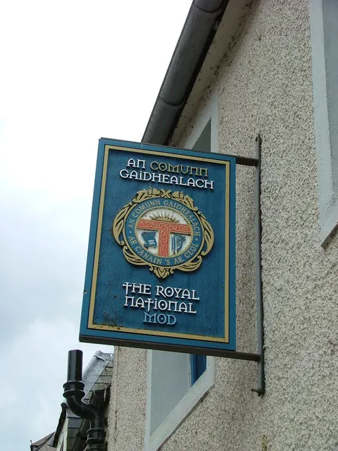 A hanging sign for An Comunn Gàidhealach reading 'The Royal National Mod' outside the festival's office in a past host town.