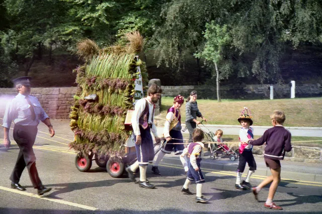 Morris dancers and children walk alongside the rush-laden Saddleworth Rushcart as it is pulled through the village.