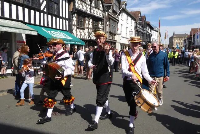Costumed musicians lead the Shakespeare's Birthday parade past half-timbered buildings on a Stratford-upon-Avon street.