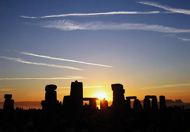 The sun rises between the stones of Stonehenge above a crowd gathered for the summer solstice.