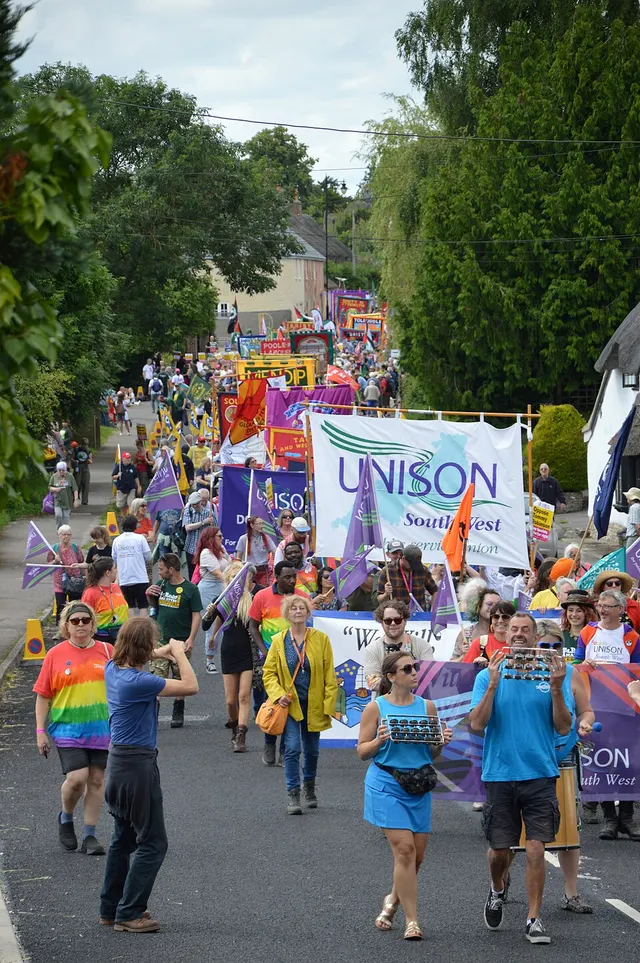A crowd of marchers carrying union banners and flags fills a village street during the Tolpuddle Martyrs' Festival.
