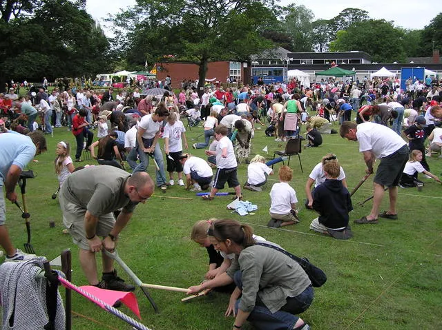 Competitors kneel on a grass field with garden forks trying to charm worms to the surface at the World Worm Charming Championships in Willaston.