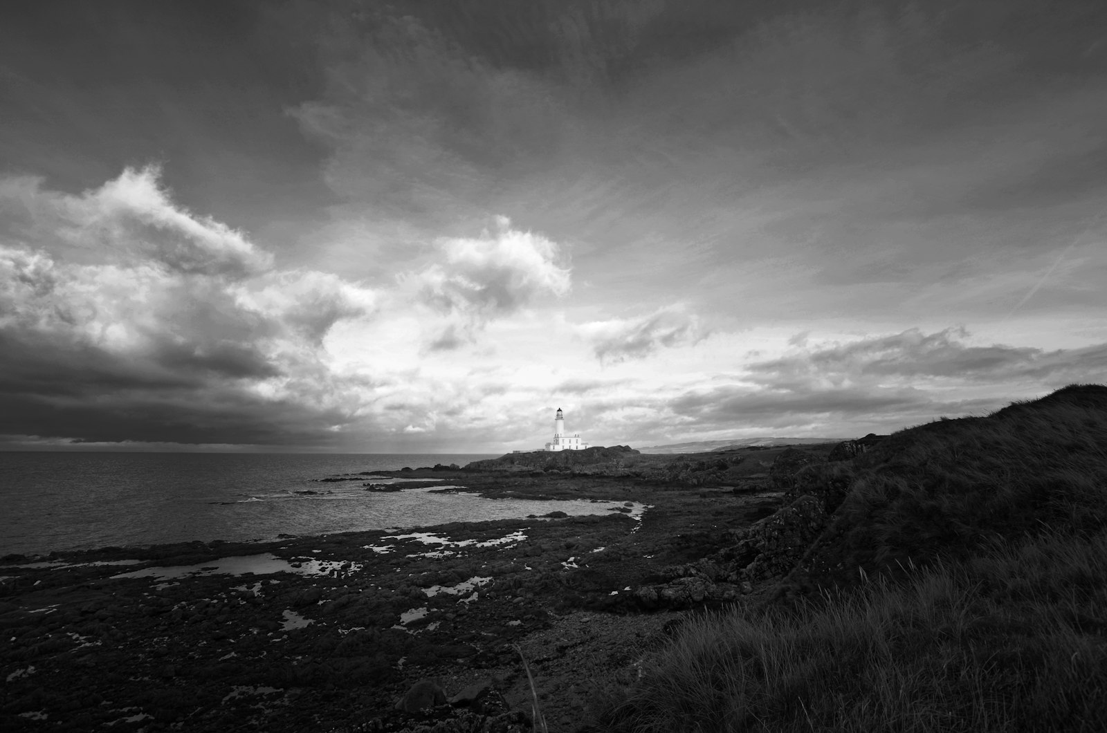 Photo of grayscale photography of lighthouse beside body of water.