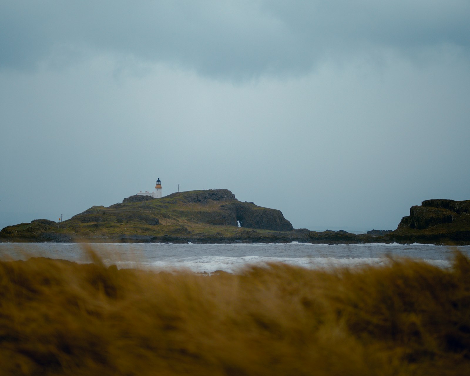 Photo of a small island with a lighthouse in the distance.