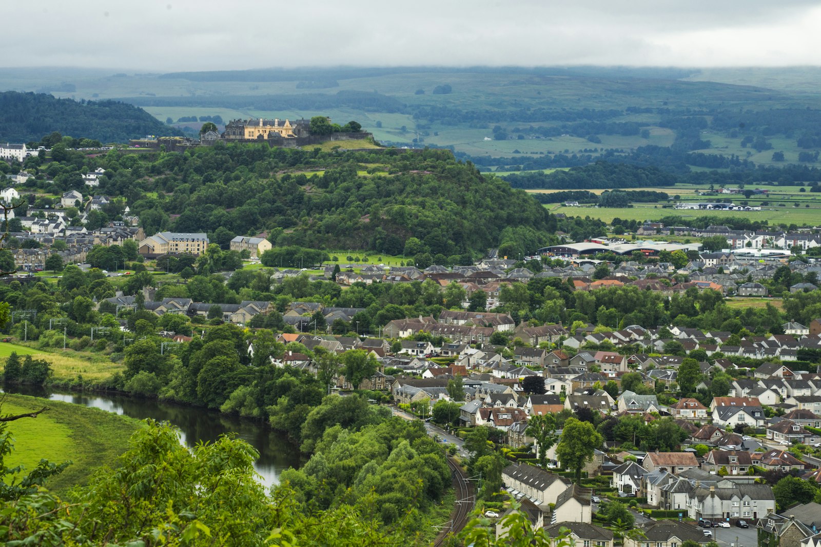 Photo of Town nestled in green valley with castle on hill.