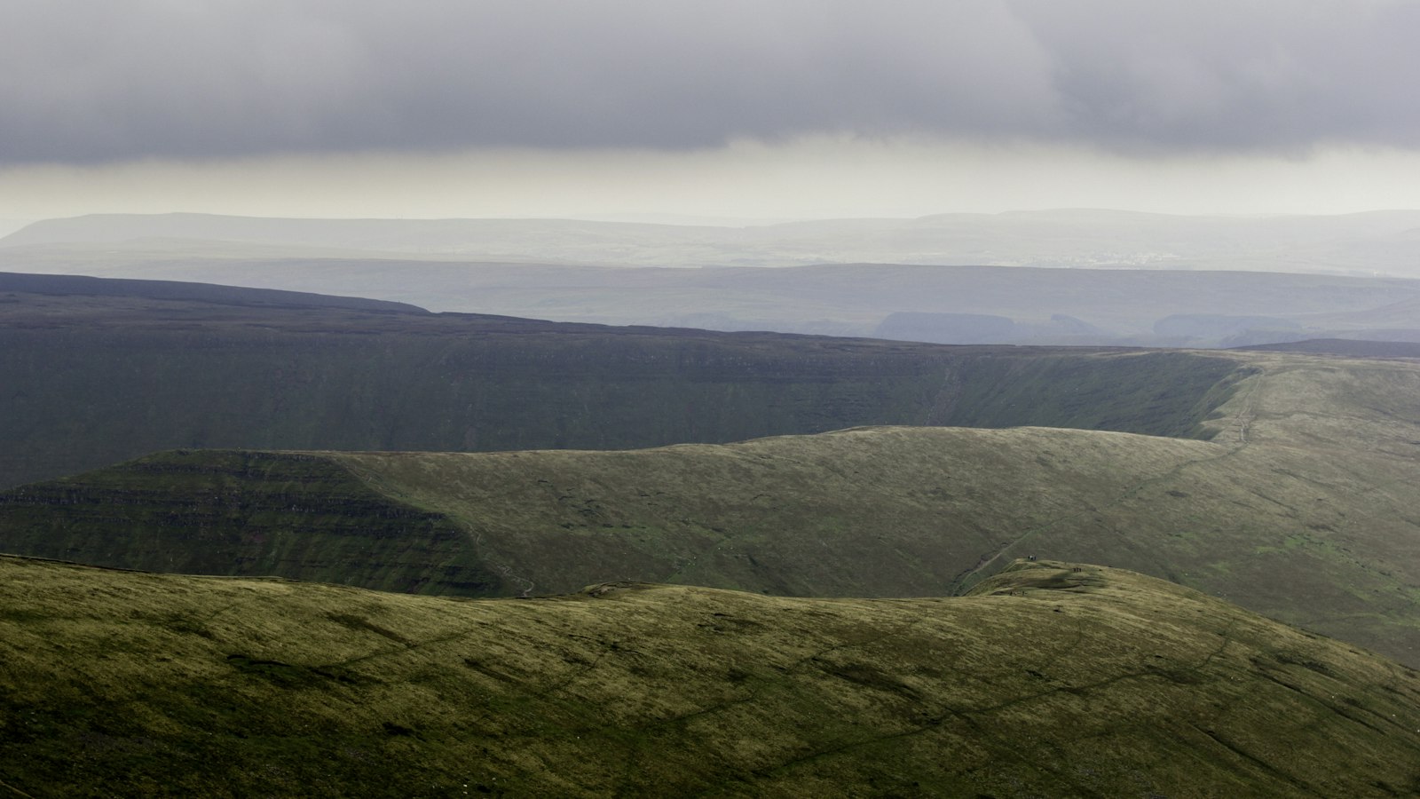 Photo of green grass covered mountain under white skies.