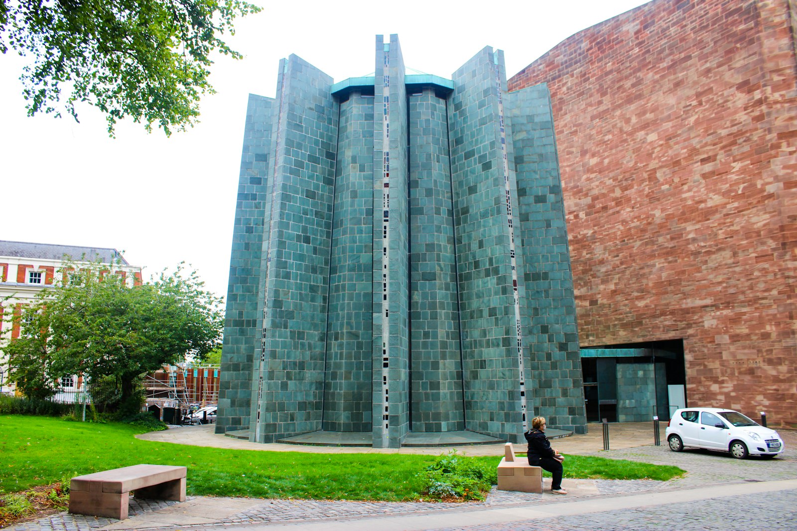 Photo of a woman walking past a tall building next to a park.